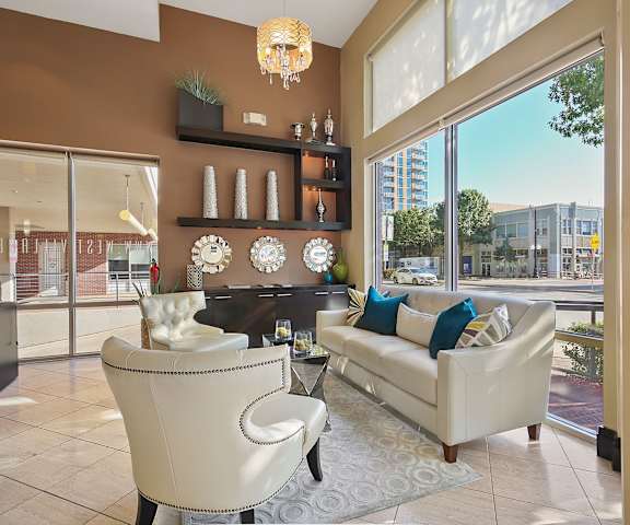 The amazing resident lounge with a beautiful white couch, decorations, large windows with curtains, white plush chairs, large sliding glass doors, and coffee tables at the Uptown Apartment Homes. 