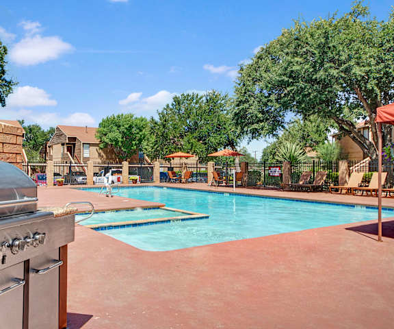 The large, turquoise outdoor pool with pool chairs, tables, grill, and chairs with the apartments in the background at Trinity Place Apartment Homes. 