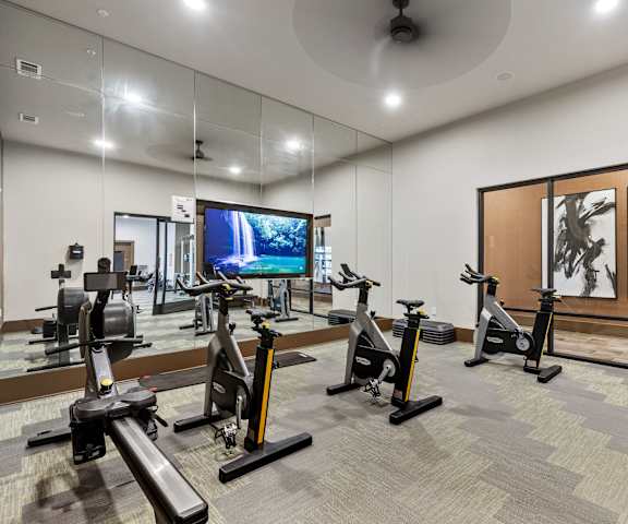 A spacious gym with exercise bikes, a mirror wall, cardio machines, windows, TVs, and weights at Waterford Market Apartment Homes. 