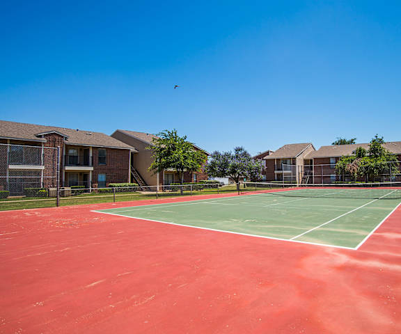 The gorgeous green and red tennis courts with the brick apartment buildings and trees in the background. 