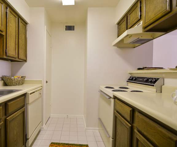 A cozy kitchen with white appliances, light counter, and large wooden cabinets at Wildflower Apartment Homes. 