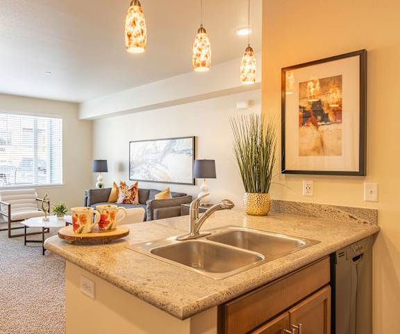  A view of the living room with a couch, coffee tables, chairs, a window from the kitchen with a sink in front at 600 Riverside. 