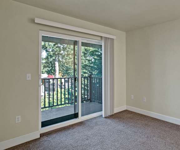 An empty living room with carpeting and a door to the balcony at Forest Hills Estates. 