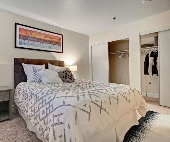 A bedroom with a queen-size bed, large closets, artwork, and nightstands at Foster Greens.  
