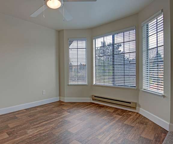 An empty living room with hardwood flooring and large windows at Foster Greens. 