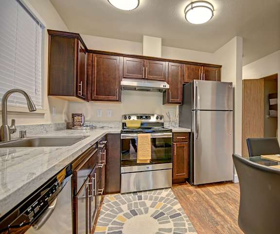 A kitchen with stainless steel appliances, marble countertops, and dark wooden cabinets at Foster Greens. 