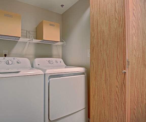 The laundry room with a washer and dryer and shelving at Foster Greens Apartments. 