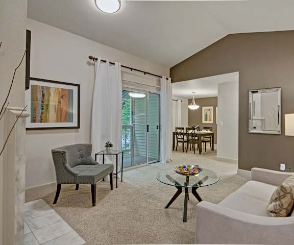 The living room with a couch, plush chairs, coffee table, decorations, doors to the balcony, a TV, and view of the dining room at Island Park. 