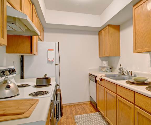 A kitchen with white appliances, light counter, and spacious wooden cabinets at Lake Park Apartments.