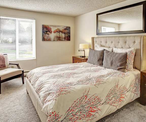 A bedroom with a queen-size bed, a dresser, decorations, window, and nightstands at Lakeside Apartments.