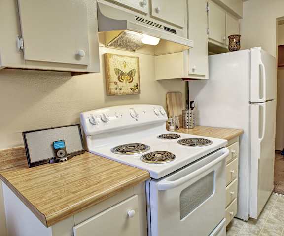 A kitchen with white appliances, light counter, and spacious wooden cabinets at Lakeside Apartments.