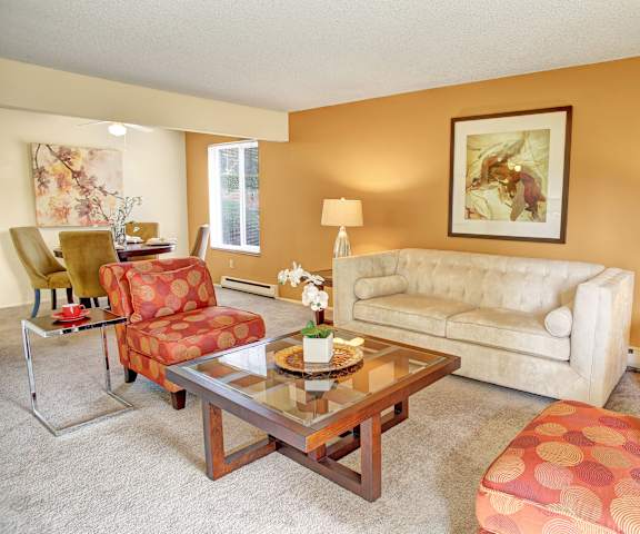 The living room with a couch, plush chairs, coffee table, decorations, and view of the dining room and the kitchen at Lakeside Apartments. 
