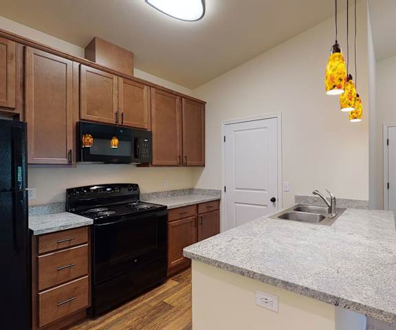 A kitchen with black appliances, marble countertops, and wooden cabinets at Leavenworth Haus Apartments. 