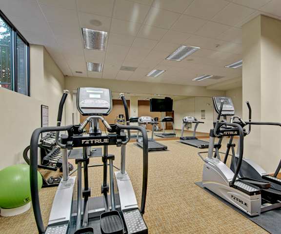 A gym with cardio machines, windows, TVs, and weights at Ondine at Juanita Bay Apartments. 