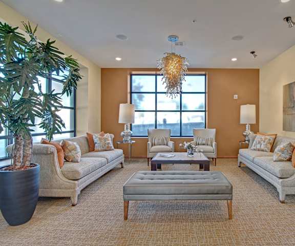 The resident lounge with a large window, plants, couches, wall art, decorations, plush chairs, and coffee tables at Ondine at Juanita Bay Apartments. 