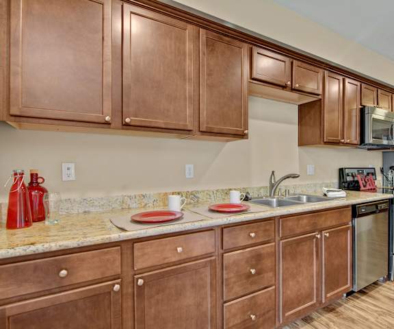 A large kitchen with two places set with plates and mugs ready for breakfast, stainless steel appliances, spacious marble countertops, and large medium stained wooden cabinets at Ondine at Juanita Bay Apartments. 