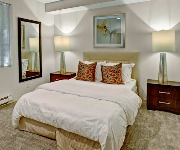 A large/cozy bedroom with a queen-size bed, a dresser, decorations, window, and nightstands at Portsmith Apartments. 