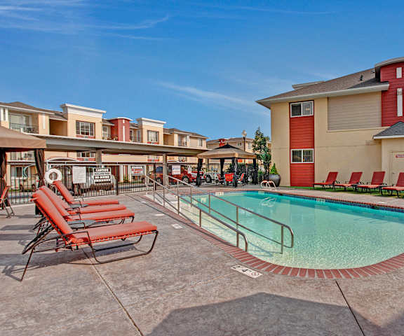 The large, turquoise outdoor pool with red pool chairs with the apartments in the background at Riverside 9 Apartment Homes. 
