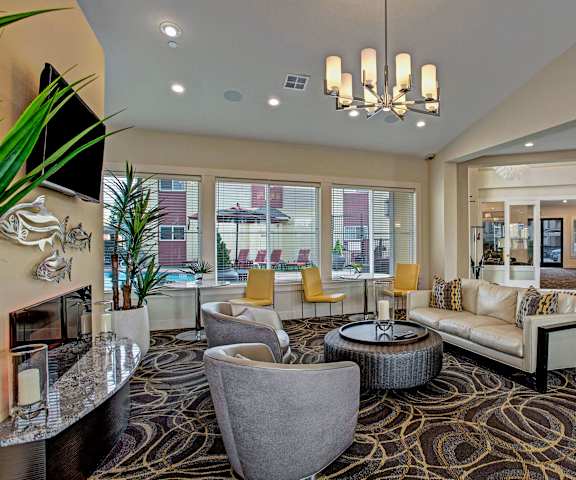 The resident lounge with tan leather couches, plush chairs, and tables and chairs by the large windows, and a cozy fireplace with a TV and fish decorations above and two plants on either side at Riverside 9 Apartment Homes. 