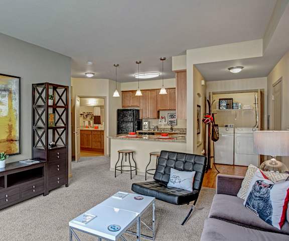 The spacious living room with a couch, a leather chair, coffee table, overhead lighting, decorations, a TV, and the kitchen at Riverside 9 Apartment Homes. 