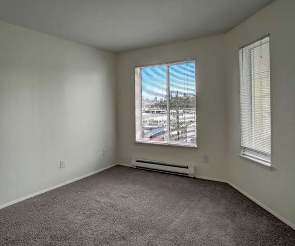An empty living room with carpeting and two windows at St. James Tower Apartments. 