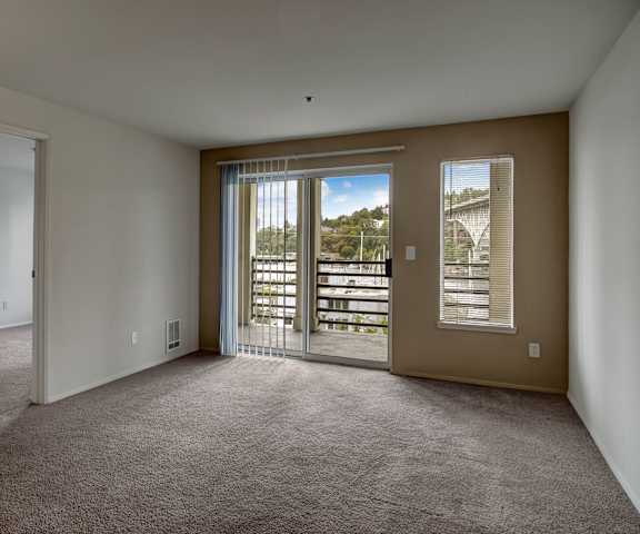 A large, empty living room with carpeting and a sliding glass door to the balcony at St. James Tower Apartments. 