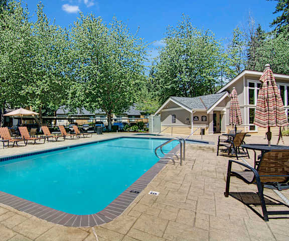 The large, turquoise outdoor pool with pool chairs, tables, and chairs with the apartments in the background at the Cove Apartment Homes. 