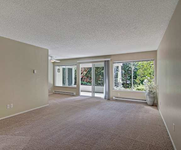 A large, empty living room with carpeting and a door to the balcony at Watercrest Apartment Homes. 