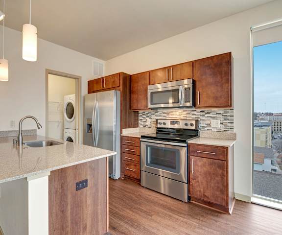 A kitchen with stainless steel appliances and a marble countertop and a laundry room in the background at Avenir Apartments. 