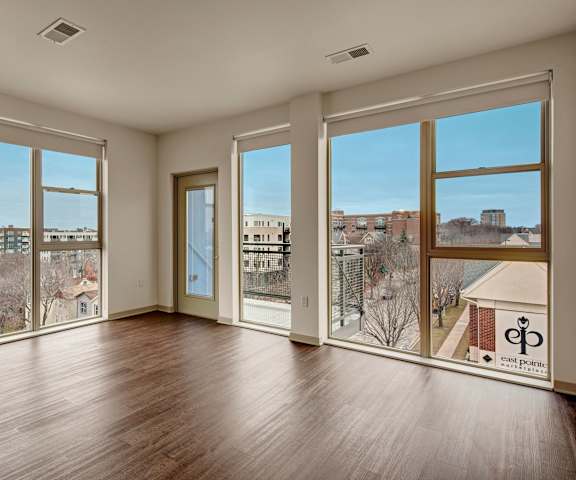 An empty living room with large windows, wood floors, and a balcony at Avenir. 