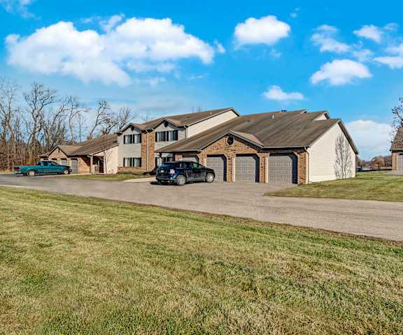 The exterior of the ivory and tan townhouse building with three garage doors, a grassy lawn, bare trees, and a road at River's Cove Apartment Homes. 