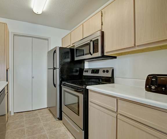 A cozy kitchen with stainless steel appliances, kitchen utensils, white countertops with lots of room, and large wooden cabinets at St. James Place Apartment Homes. 