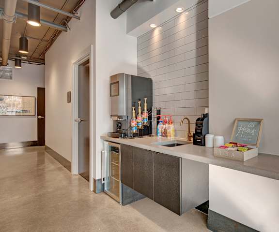 The gray coffee station with a coffee machine, coffee options, flavorings, and tea options on top of a gray counter at Stitchweld Apartment Homes. 