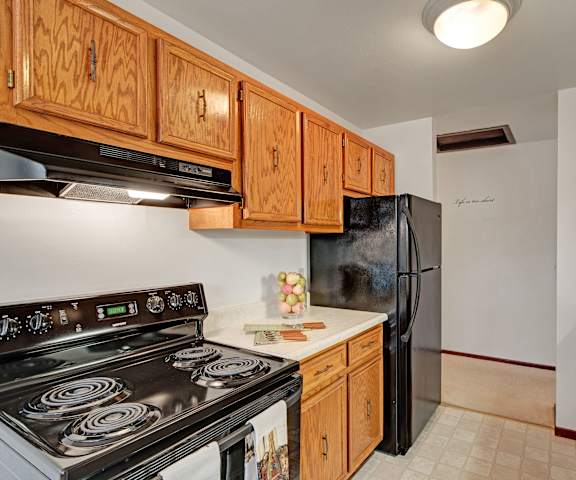 A cozy kitchen with black appliances, light countertops with lots of room, overhead lights, and wooden cabinets with decorations at Sunset Ridge Apartment Homes. 