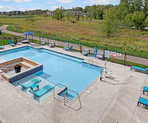 The large, turquoise outdoor pool with blue pool chairs with greenery, trees, and the apartments in the background at the Lafayette Apartment Homes. 