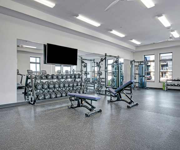 A spacious gym with cardio machines, windows, TVs, and weights at the Lafayette Apartment Homes. 