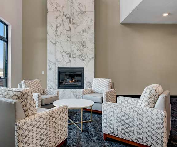 The amazing, white and tan resident lounge with a fireplace, decorations, large windows with curtains, plush, white, floral-patterned chairs, and coffee tables at the Lafayette Apartment Homes. 