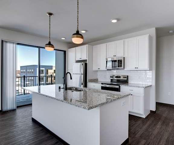 A large, modern kitchen with stainless steel appliances, kitchen utensils, granite countertops with lots of room, a kitchen island, and large white wooden cabinets at the Lafayette Apartment Homes. 