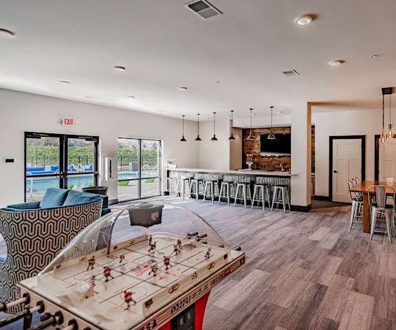A resident lounge with a light blue couch, an air hockey game table, a light wooden table and metal chairs, and a bar counter with barstools at the Park Apartment Homes. 
