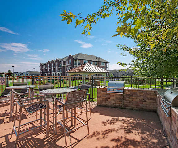 The fun patio with a grilling area, table and chairs, and green space with the apartments in the background at Van Buren Place Apartment Homes. 