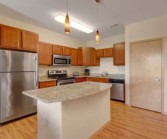 A large, modern kitchen with stainless steel appliances, granite countertops with lots of room, a granite island, and large wooden cabinets at Van Buren Place Apartment Homes. 