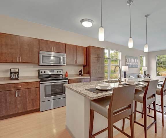 A large, modern kitchen with stainless steel appliances, bar counter with barstools, kitchen utensils, marble countertops with lots of room, and large wooden cabinets at The Vue at Pinnacle Park Apartment Homes. 