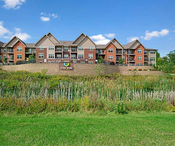 The exterior view with multiple brown, tan, and burnt orange buildings and a grassy field in front at the Vue at Pinnacle Peak Apartment Homes. 