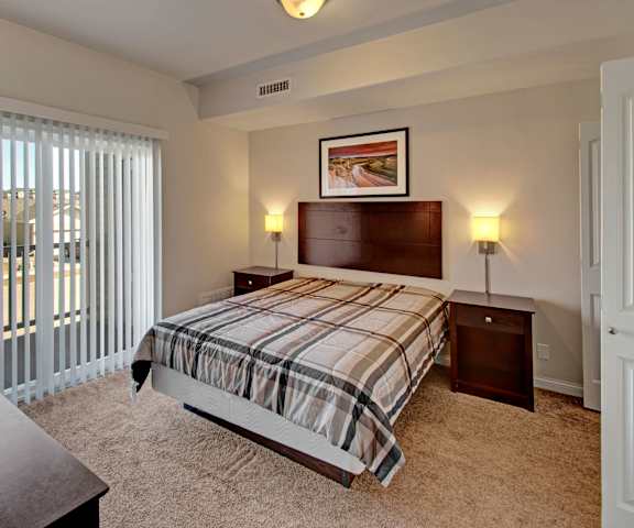 A bedroom with a queen-size bed, closet, and nightstands at Confluence at Harvest Hills. 