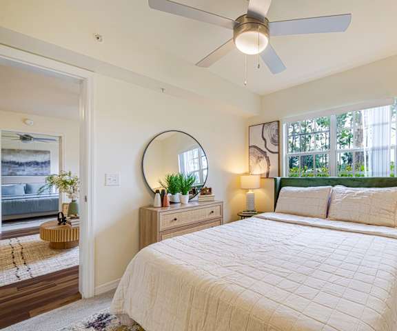 A bedroom with a large bed, a ceiling fan, and a mirror on the wall.
