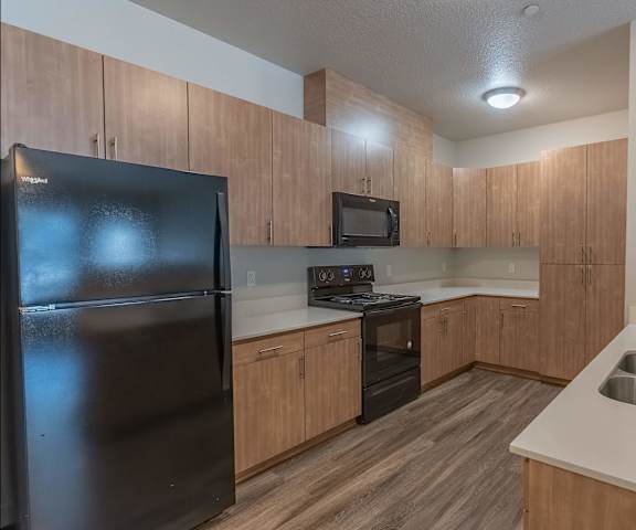 A kitchen with a black refrigerator, wooden cabinets, and a stainless steel sink at Sandyplace Apartment Homes, Sandy, OR