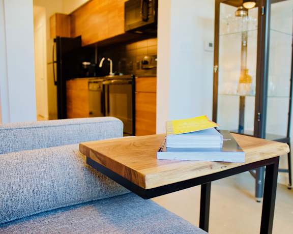 A grey couch sits in front of a wooden coffee table with a book and a yellow card on it.