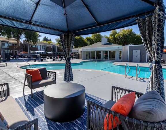 A poolside area with a round table and chairs under a canopy.