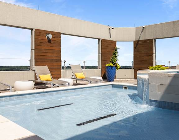 A pool with a waterfall and a chair with a yellow cushion at Clayton on the Park Apartments, Clayton, Missouri
