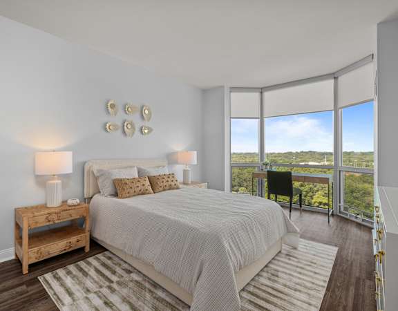 A bedroom with a large bed and a view of the outdoors through the window at Clayton on the Park Apartments, Clayton, Missouri